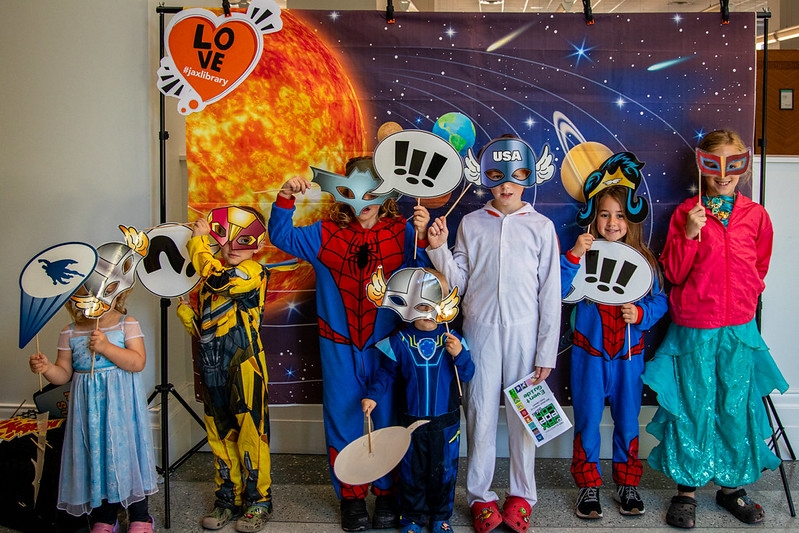 Children in costumes, in front of a themed backdrop. They are holding props.