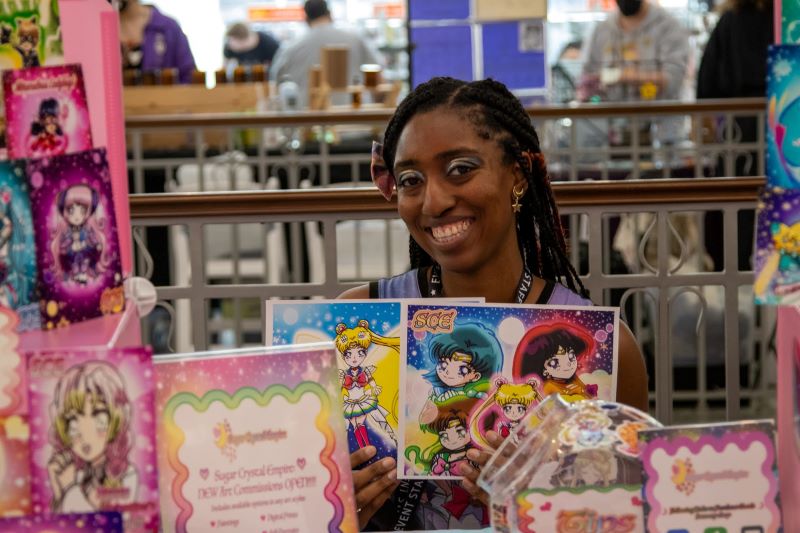 Photo of an artist alley vendor, surrounded by Sailor Moon inspired fan art prints