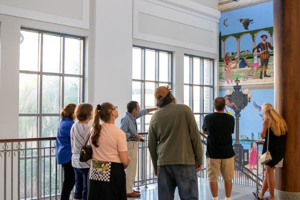 A volunteer docent leads an art tour through the Main Library. He's pointing out a mural in the stairwell.