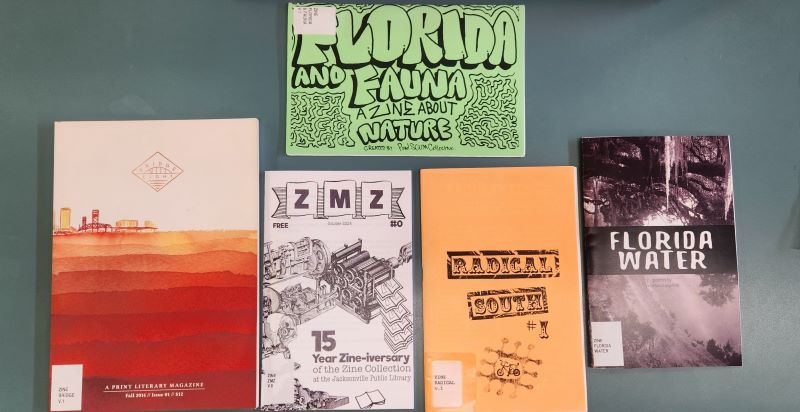 A photo of five zines with stickers on the bottom left-hand side of the cover showing library call numbers.