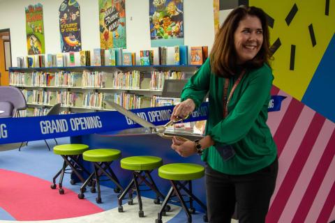 Library staff member cutting a blue ribbon at entrance to the Children's room