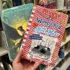 A hand holding 2 books: Percy Jackson and the Olympians and Diary of a Wimpy Kid Hot Mess.